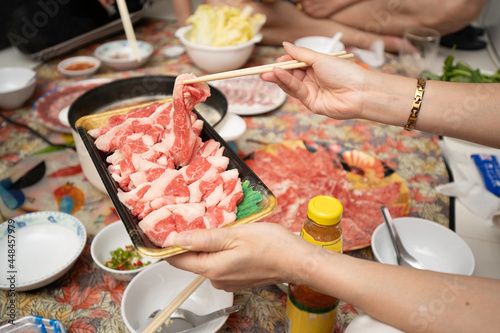 Hands of diversity people using chopsticks to pick up raw sliced beef for eating Shabu Shabu or Sukiyaki dipping and dropping