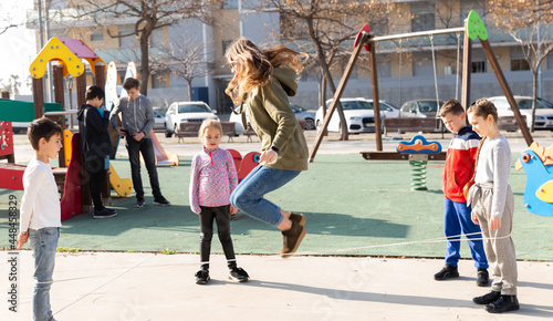 Fotografia Positive children skipping on chinese jump rope on playground