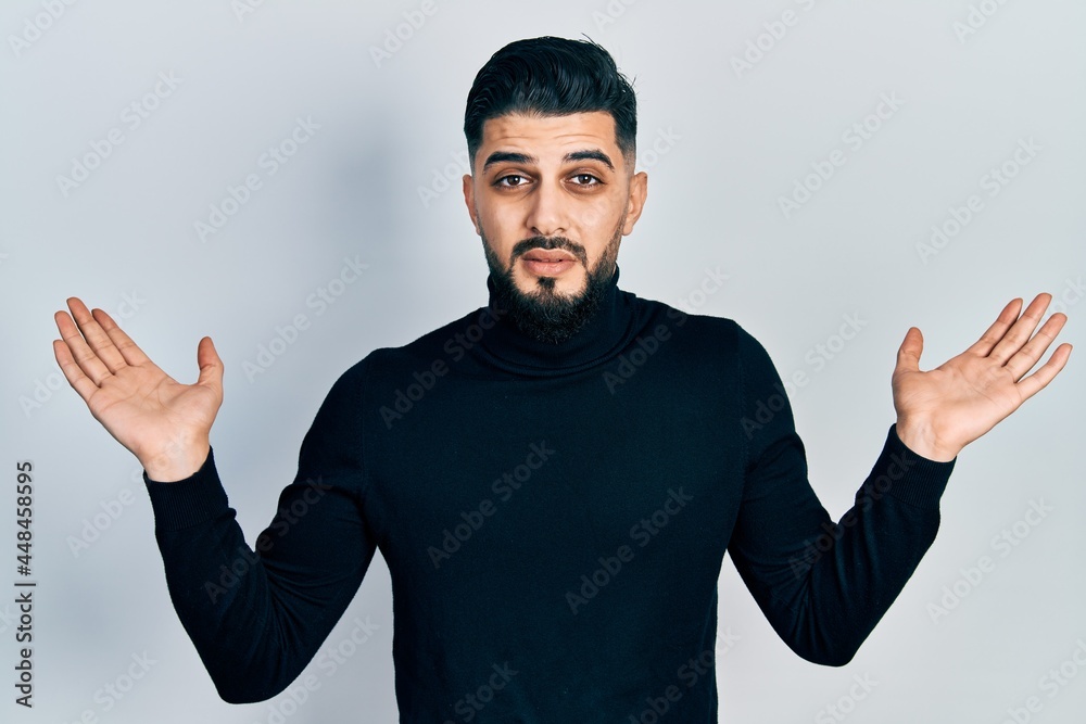 Fototapeta premium Handsome man with beard wearing turtleneck sweater clueless and confused with open arms, no idea and doubtful face.