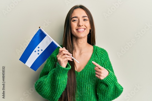 Young hispanic girl holding honduras flag smiling happy pointing with hand and finger
