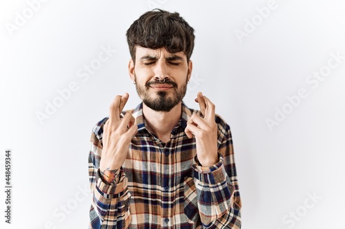 Hispanic man with beard standing over isolated background gesturing finger crossed smiling with hope and eyes closed. luck and superstitious concept.