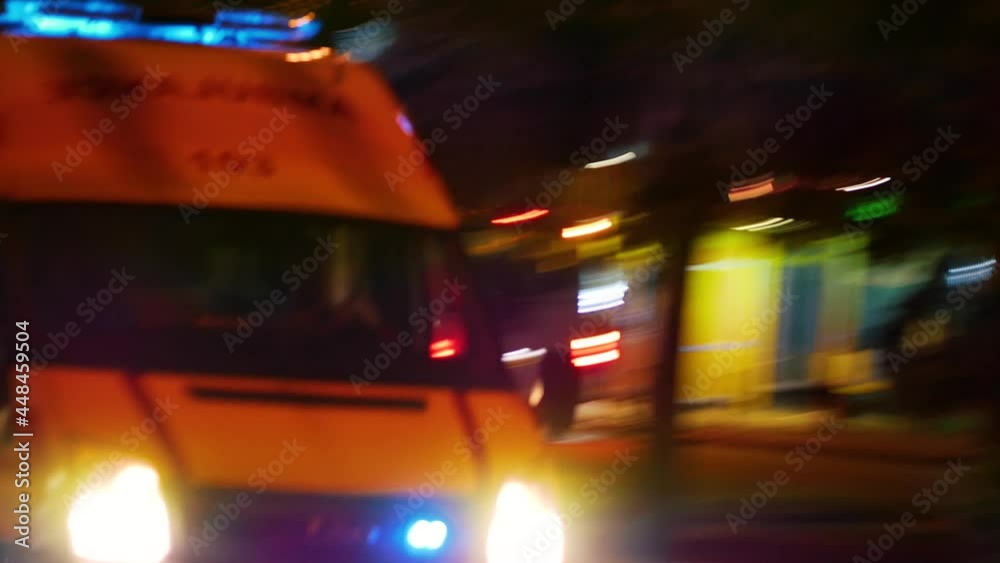 An ambulance with flashing beacons on rushes along a city street at night. The car rushes to the call. The COVID-19 pandemic. Delta strain. The third wave of the incidence of coronavirus infection.
