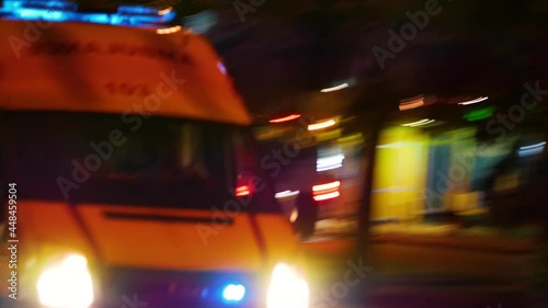 An ambulance with flashing beacons on rushes along a city street at night. The car rushes to the call. The COVID-19 pandemic. Delta strain. The third wave of the incidence of coronavirus infection.