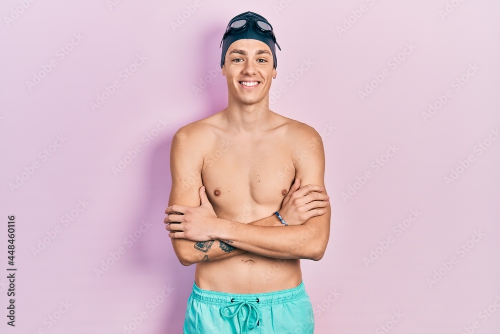Young hispanic man wearing swimwear and swimmer glasses happy face smiling with crossed arms looking at the camera. positive person.