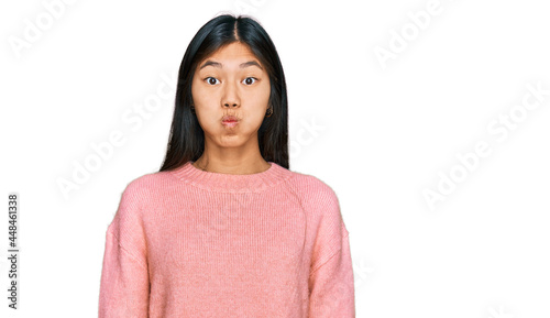 Beautiful young asian woman wearing casual winter sweater puffing cheeks with funny face. mouth inflated with air, crazy expression.