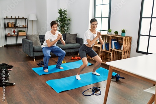Young caucasian couple smiling happy training legs exercise with dog at home.