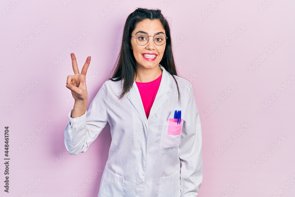 Young hispanic girl wearing scientist uniform smiling with happy face winking at the camera doing victory sign. number two. Young hispanic girl wearing scientist uniform smiling with happy face winking at the camera doing victory sign. number two.