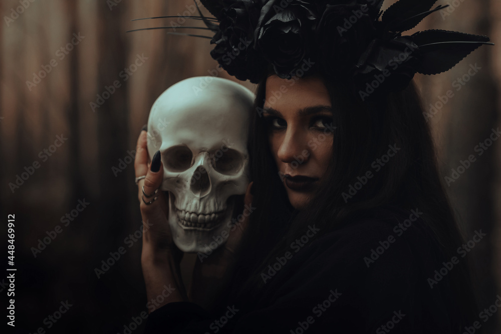 frightening evil witch in black rags holds a dead man's skull in her hands for a dark ritual