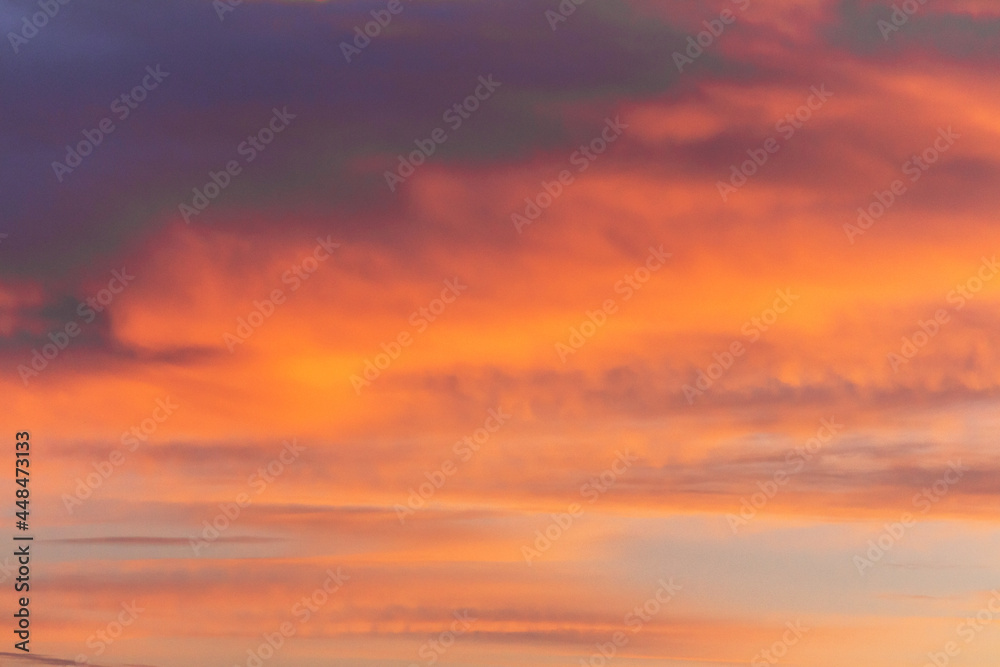 Colorful dramatic sky at sunset with layered rain clouds of purple and gold color