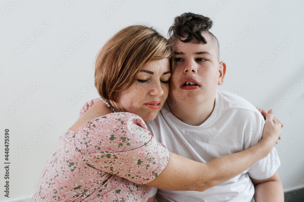 Mother hugging disabled boy 17 years old in wheelchair with cerebral palsy over white background. Woman assists person with Special Needs. Emotional family lives with disability, holding hands Mother hugging disabled boy 17 years old in wheelchair with cerebral palsy over white background. Woman assists person with Special Needs. Emotional family lives with disability, holding hands