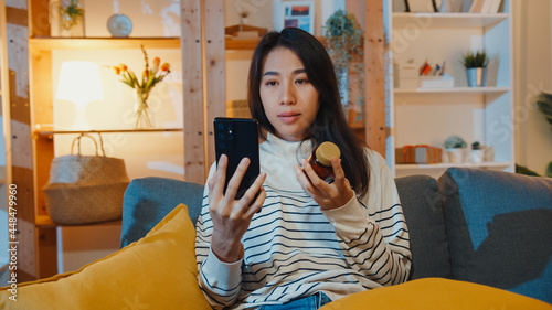 Fotografie Sick young Asian lady hold medicine sit on couch video call with phone consult with doctor at home night
