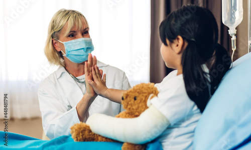 Woman doctor wearing protective mask service help support discussing and consulting talk to little girl patient and giving hi five check up information in hospital