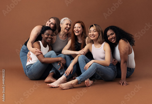 Portrait of six laughing women of different ages and body types sitting together on a brown background in studio photo