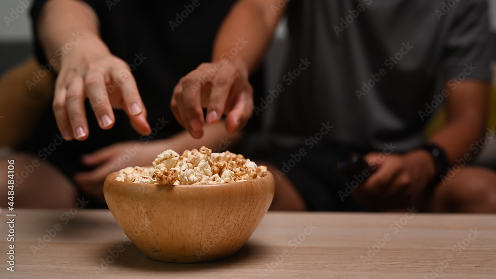 Close up view two men sitting on couch and eating popcorn.