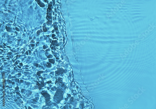 Transparent blue water surface with ripples and splashes. Summer water waves background in sunlight. copy space