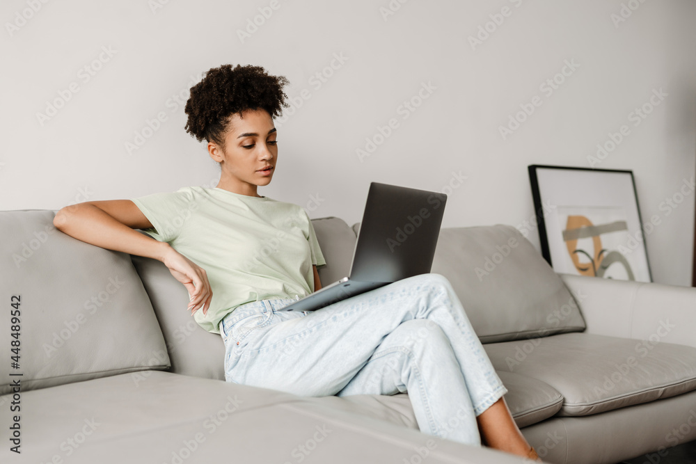 Young black woman working with laptop while sitting on couch at home Young black woman working with laptop while sitting on couch at home