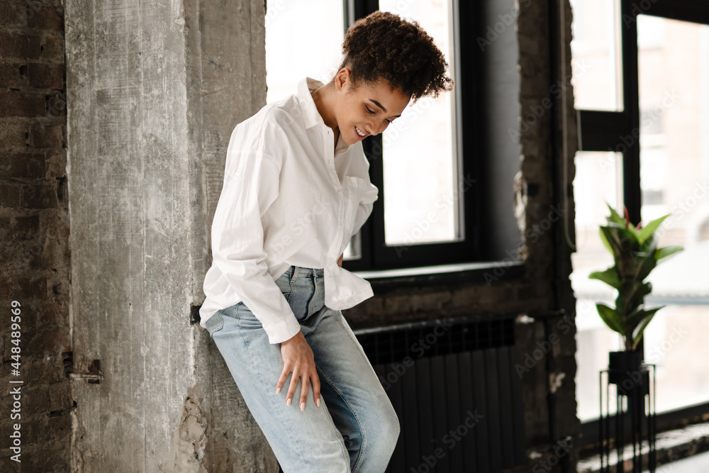 Young black woman laughing while leaning on wall indoors Young black woman laughing while leaning on wall indoors