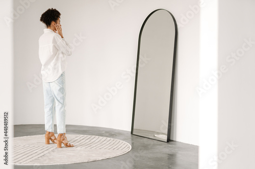 Young black woman standing and looking at mirror indoors photo