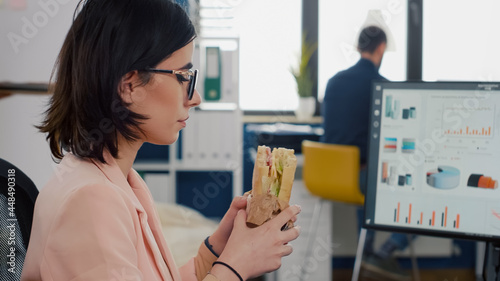 Foto Entrepreneur woman eating tasty sandwich during takeout lunchbreak working at financial graphs in startup business company office