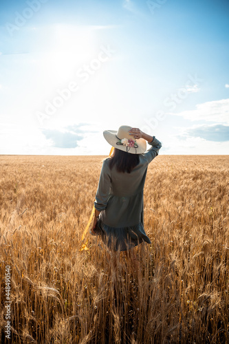 A girl walks through a field in wheat in a wicker hat and a dress. Unity with nature, inspiration.