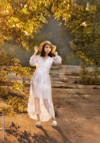 A young girl in a park in a white dress and a hat