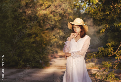 A young girl in a park in a white dress and a hat