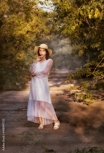 A young girl in a park in a white dress and a hat