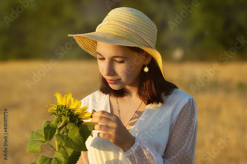 A young girl in a wheat field with a sunflower flower in summer at sunset