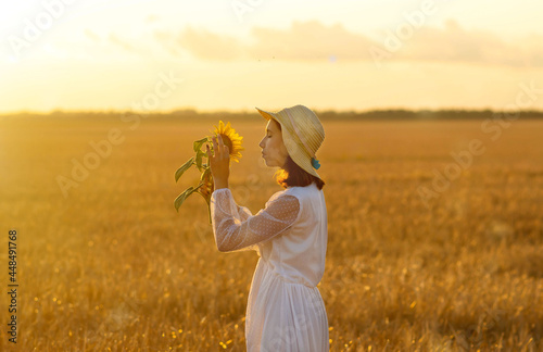 A young girl in a wheat field with a sunflower flower in summer at sunset