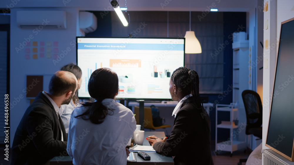 Businesswoman explaining financial graphs using presentation monitor overworking in office meeting room in evening. Diverse multi-ethnic teamwork brainstorming company strategy at night Businesswoman explaining financial graphs using presentation monitor overworking in office meeting room in evening. Diverse multi-ethnic teamwork brainstorming company strategy at night