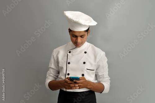 Portrait of a happy male chef dressed in uniform holding Mobile and sending SMS or chatting 
