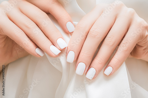 Female hands with white nail design. Glitter white nail polish manicure. Woman hands on white fabric background.