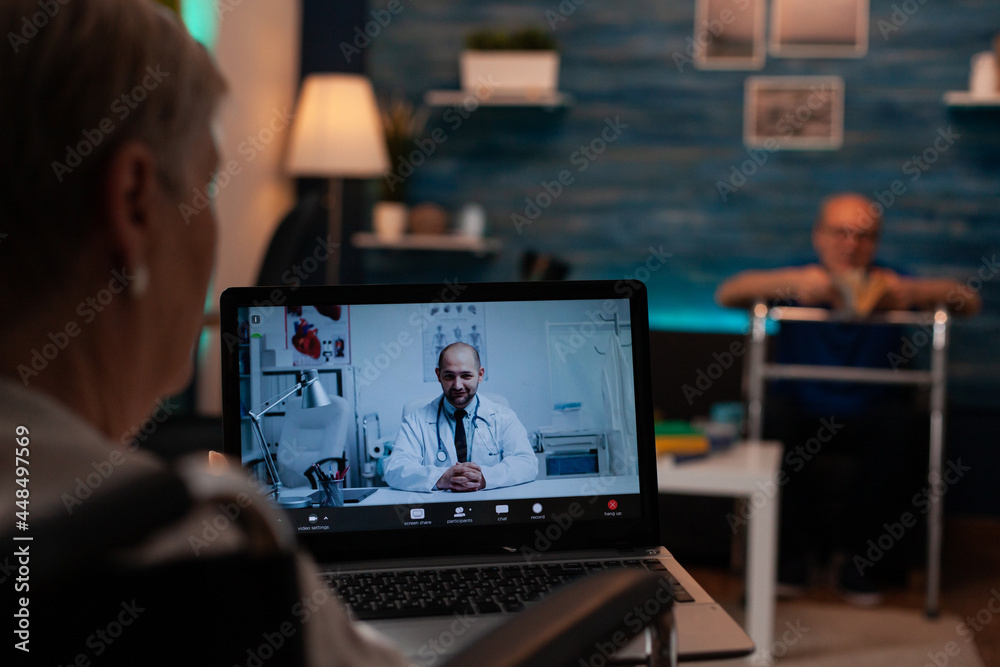 Old woman talking to doctor on video call conference for remote consultation on laptop computer to receive prescription medicine and advice. Elder man with walk frame sitting on couch Old woman talking to doctor on video call conference for remote consultation on laptop computer to receive prescription medicine and advice. Elder man with walk frame sitting on couch