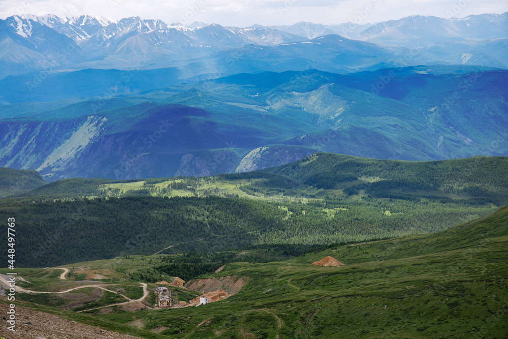 Fototapeta premium A destroyed administrative multi-storey brick building in a mountain valley. Summer landscape in the Altai Republic in Russia. Remains of a mine for the extraction of minerals.