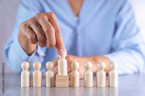 A businesswoman's hand is choosing a different level wooden puppet. to represent the selection of leaders and business planning