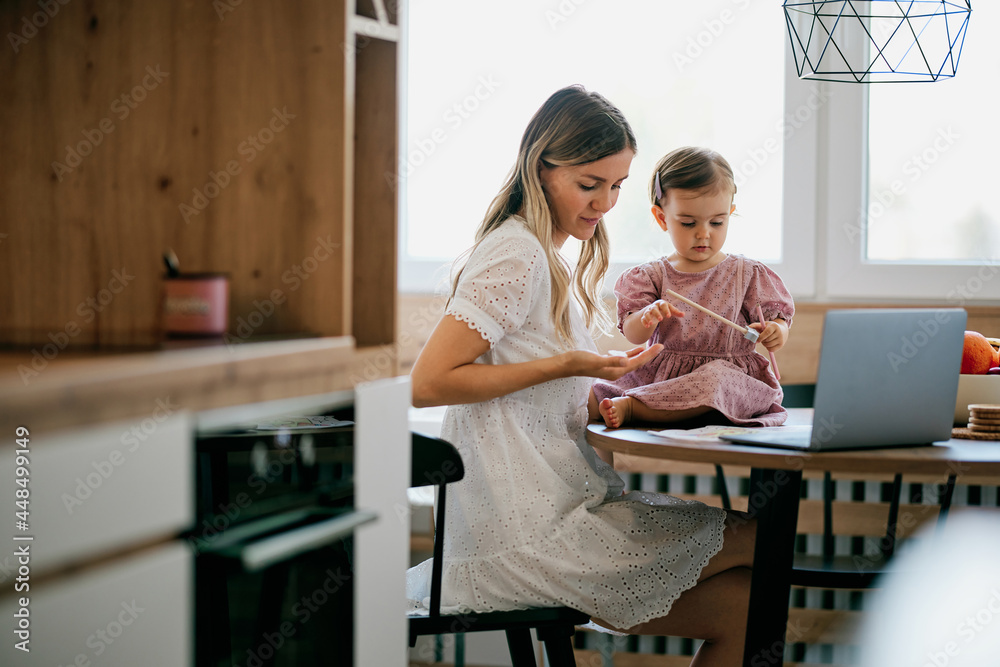 Stay at mother home sitting in kitchen and getting work done while her baby girl helping her. Stay at mother home sitting in kitchen and getting work done while her baby girl helping her.