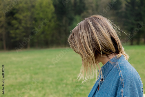 Side view on head of blond woman with forest and meadow on background