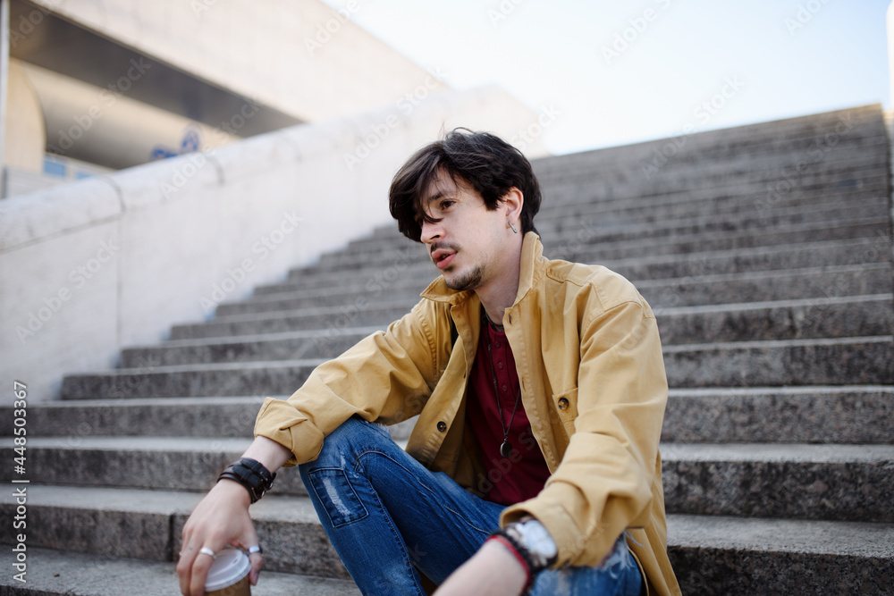 Portrait of sad young man sitting on staircase outdoors in city, resting.