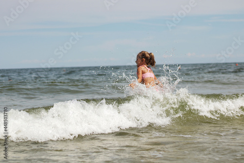 Little girl in a swimsuit splashes on the waves in the Baltic Sea.