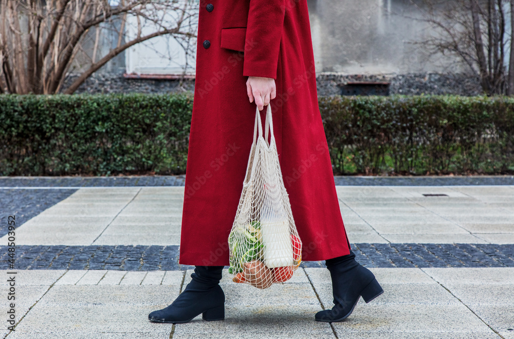 Style woman in red coat and net bag waking home after shopping.