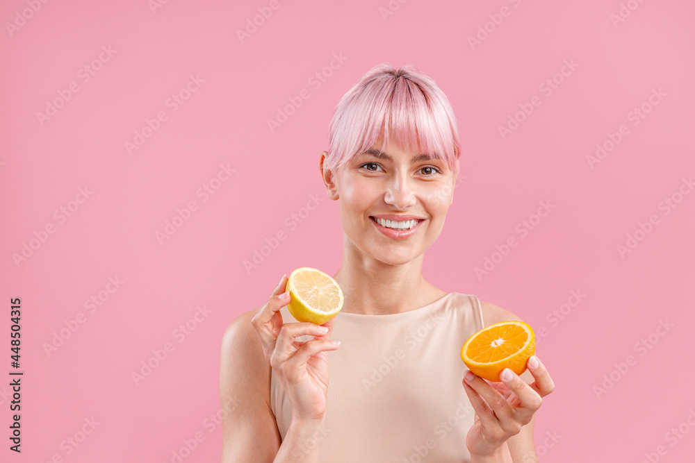 Portrait of smiling woman with pink hair holding half of fresh orange and lemon, posing isolated over pink background. Beauty, healthy eating concept Portrait of smiling woman with pink hair holding half of fresh orange and lemon, posing isolated over pink background. Beauty, healthy eating concept