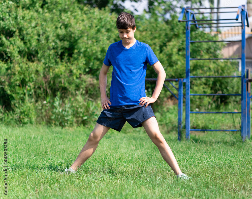teenage boy exercising outdoors, sports ground in the yard, he squats and does a warm-up, healthy lifestyle teenage boy exercising outdoors, sports ground in the yard, he squats and does a warm-up, healthy lifestyle