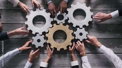 Teamwork business people concept. Different hands of men and women connect gears into working mechanism on wooden table background.