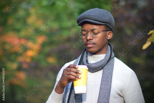 Portrait of sad depressed frustrated upset black guy, handsome African Afro American young man walking in golden autumn park in hat, scarf and glasses with cup of coffee , feeling bad, unhappy 