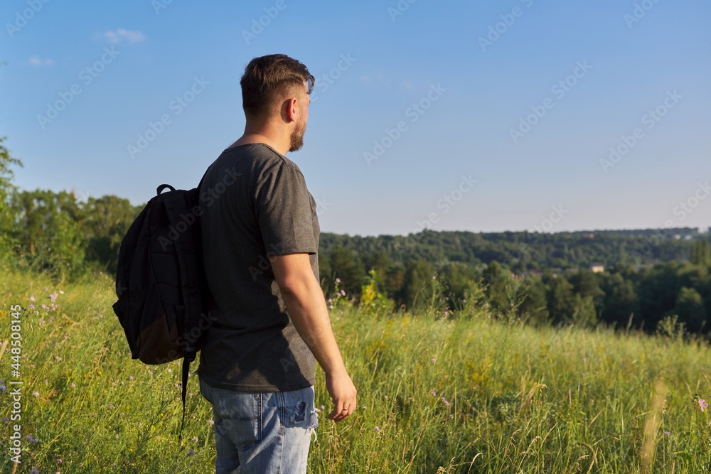 Back view of middle-aged man with backpack looking in distance at natural hills