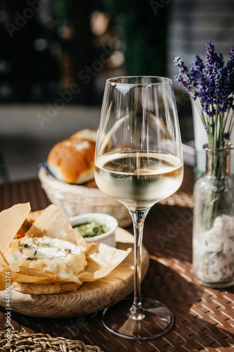Fotografie Glass of cold white wine and oven baked camembert cheese with rosemary on baking paper on wooden plate