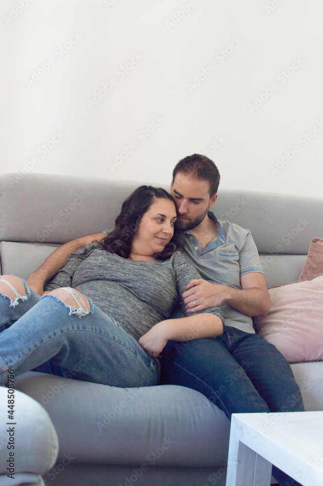 Pregnant wedding couple sitting on a sofa looking at each other and smiling Pregnant wedding couple sitting on a sofa looking at each other and smiling