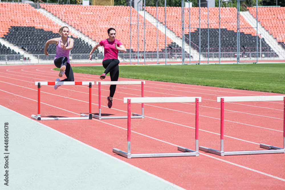 Fototapeta premium Two female sportswomen are jumping over an obstacle. Running with hurdles. Active lifestyle