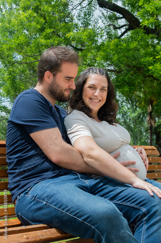 Pregnant couple sitting on a bench and posing in a park