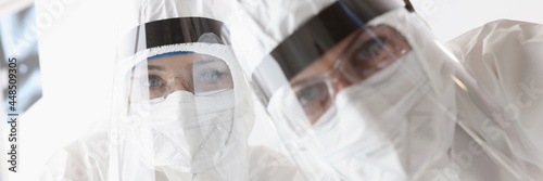 Doctors in protective antiplague suits and screens looking at patient photo
